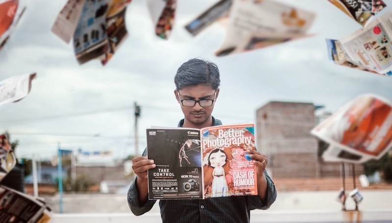 Magazine pages swirl around a person reading