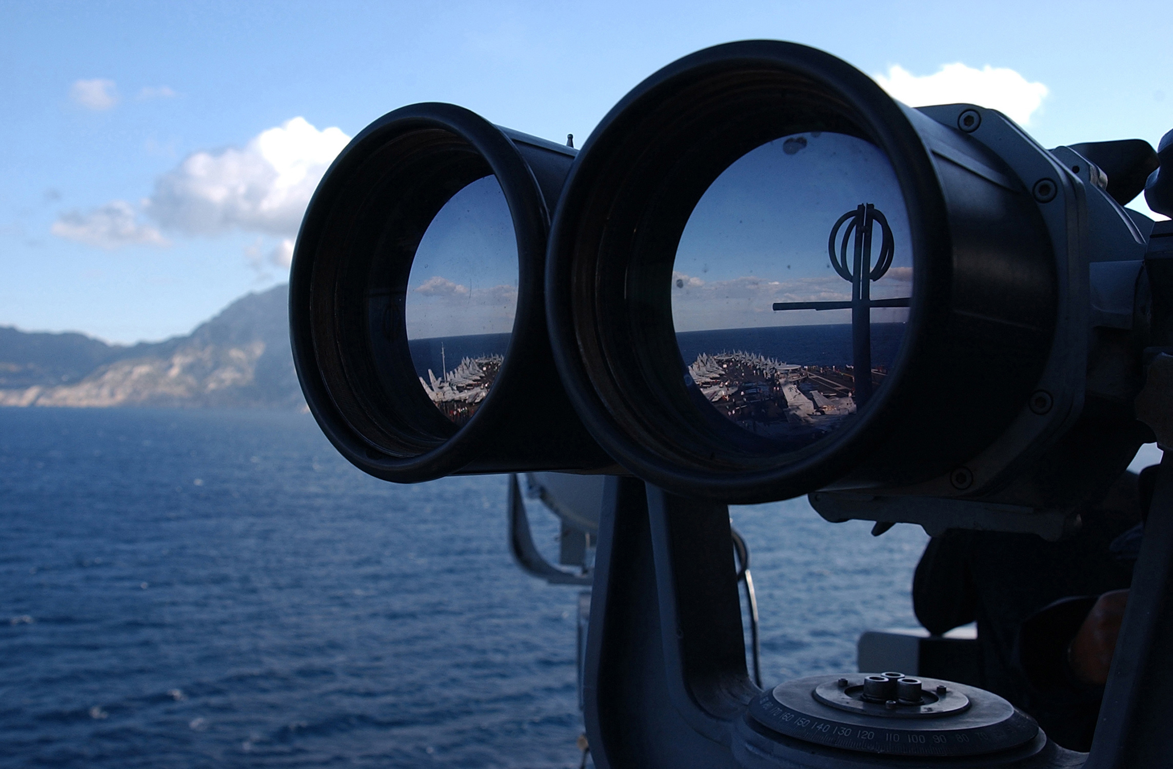 Photograph of binocular lenses from front, reflecting 2 views of an aircraft carrier